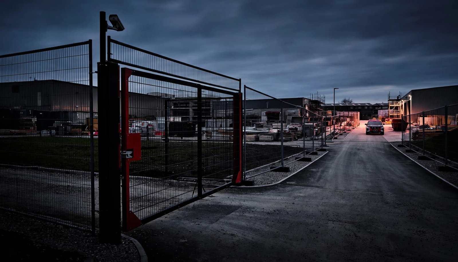 An industrial site with fencing, a security gate, and a distant patrol vehicle.