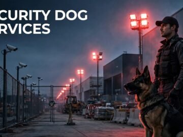 A security dog and handler patrol a fenced construction site at dusk.