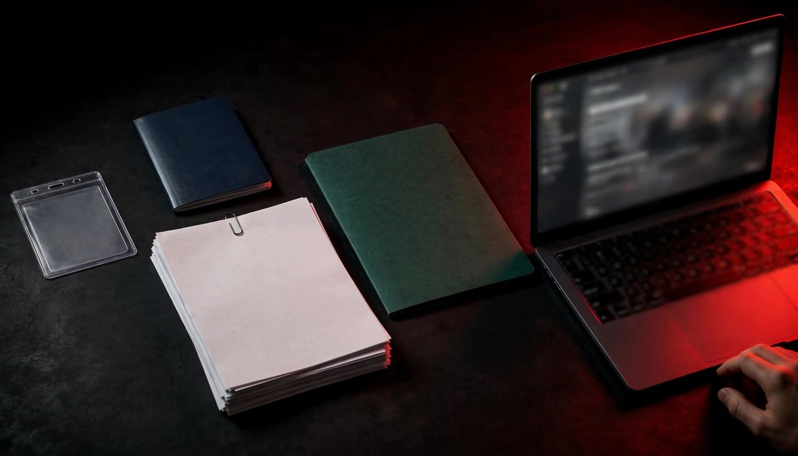 Documents, a passport, card holder, certificate folder, and laptop arranged on a dark office table.
